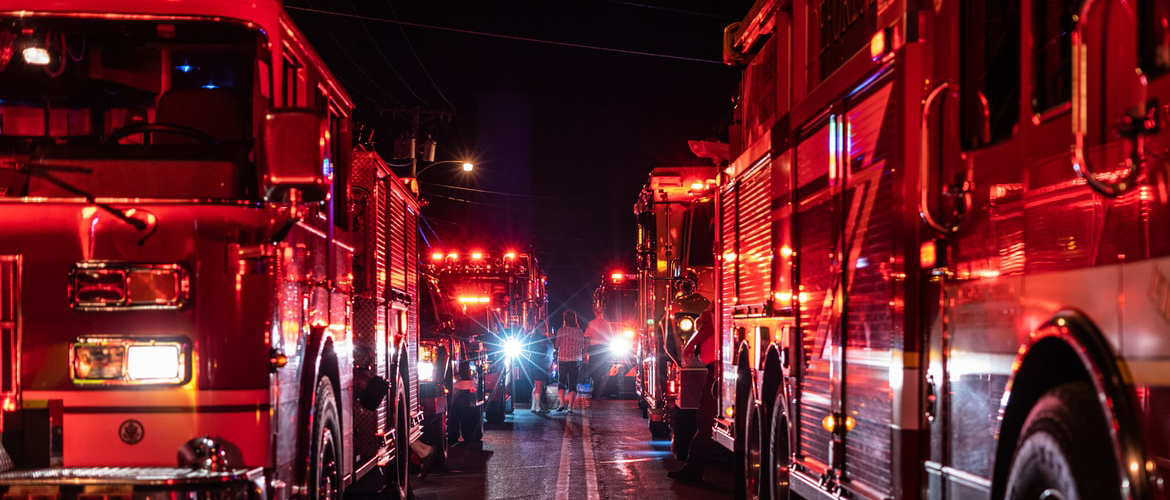 A row of firetrucks with people standing in the middle.
